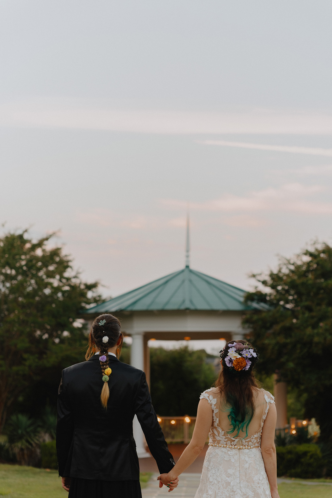 Wide cinematic shot of a bride and groom walking toward a gazebo at sunset